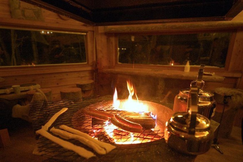 A wood-burning stove with logs, a pot, and a window in a cozy interior setting. 3