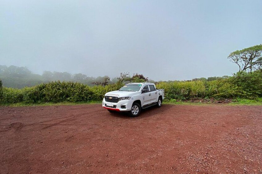 A white SUV parked on a dirt road with a foggy background and greenery. 5
