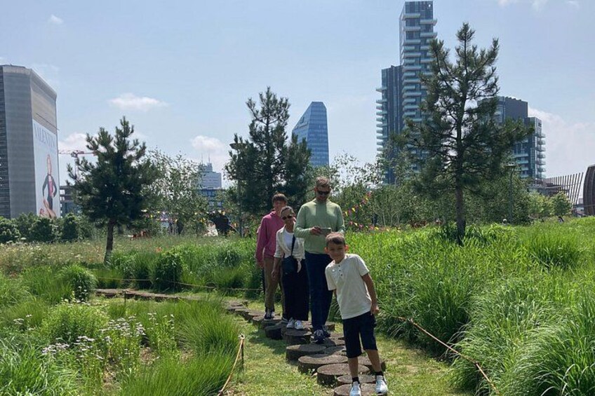 A group of people walking on a stone path in a park with tall buildings in the background. 3
