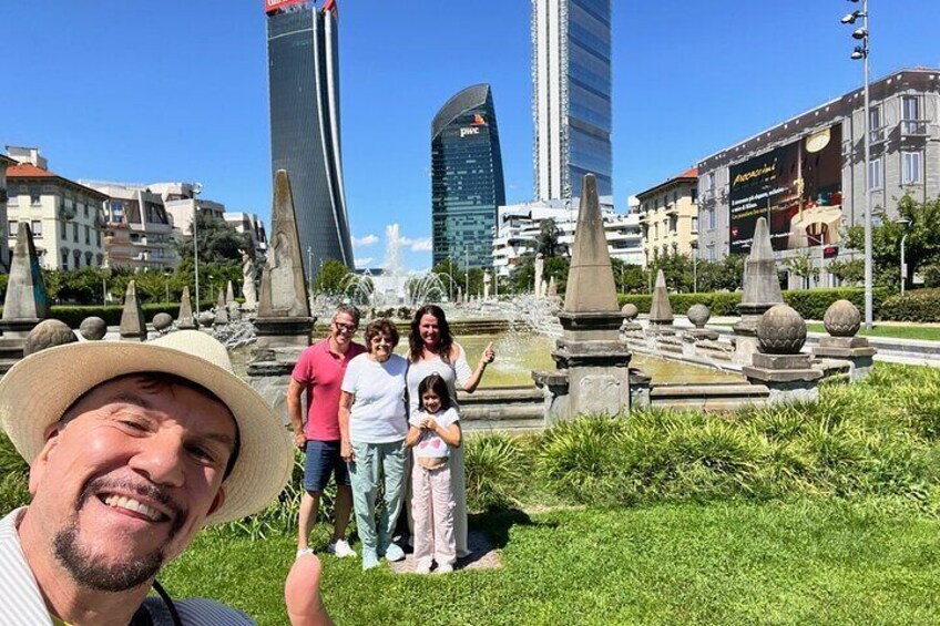 A family in a park with a fountain and modern buildings in the background. 1