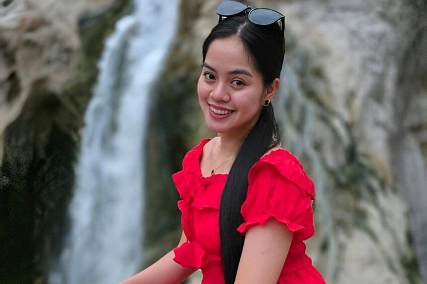Una persona con un vestido rojo y mangas fruncidas de pie frente a una cascada. 3