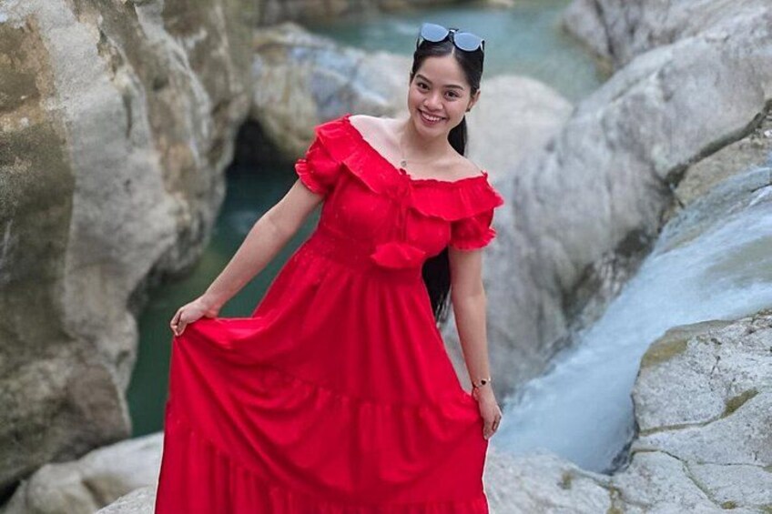 Una persona con vestido rojo de pie cerca de un arroyo pedregoso. 2