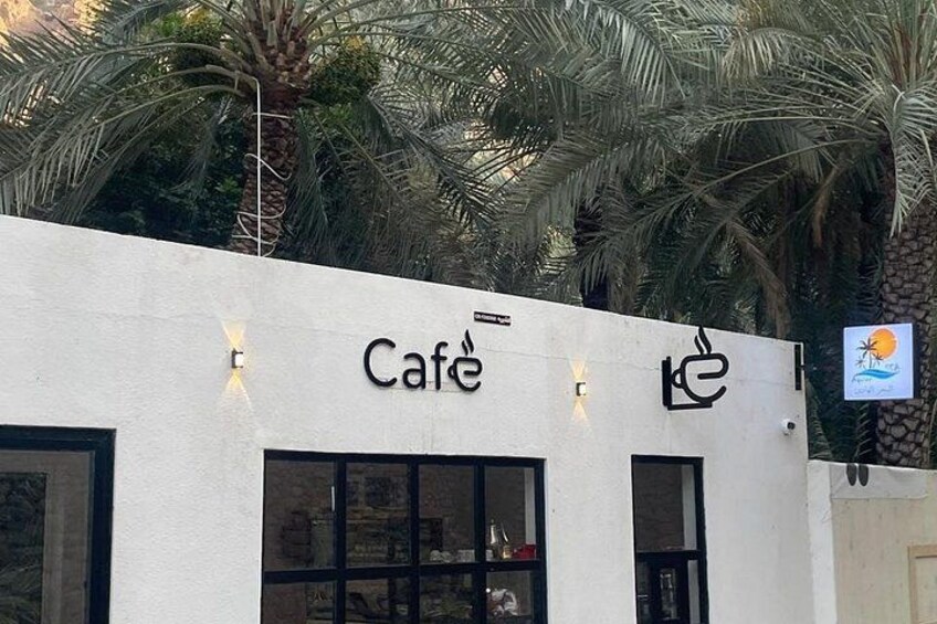 Una cafetería con fachada moderna, palmeras y un letrero con una palmera y un sol. 5