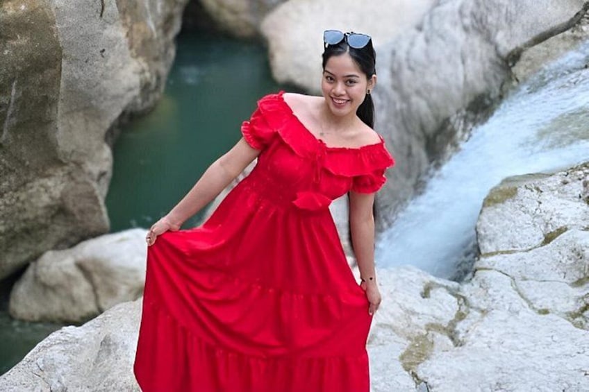 A person in a red dress standing near a rocky area with a water stream. 1