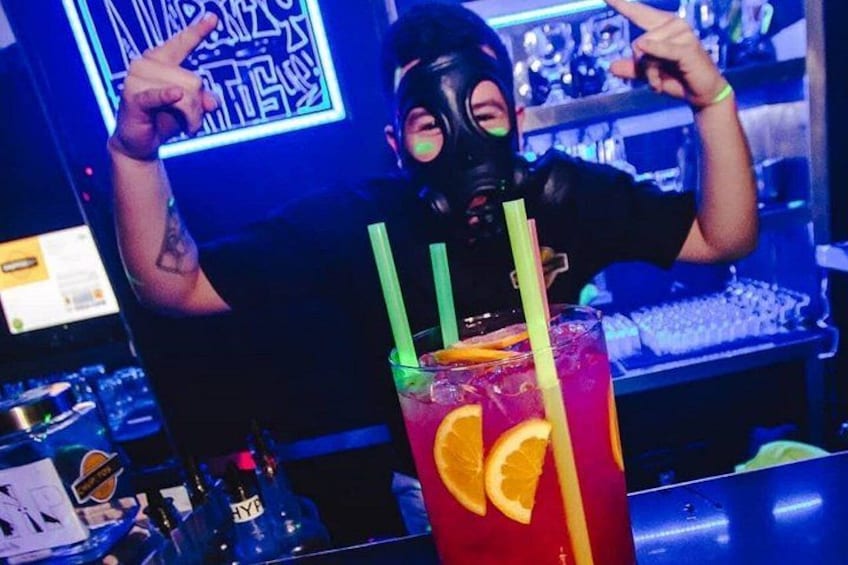 Una persona sosteniendo una bebida con pajita, un letrero de neón al fondo y una barra con botellas. 2