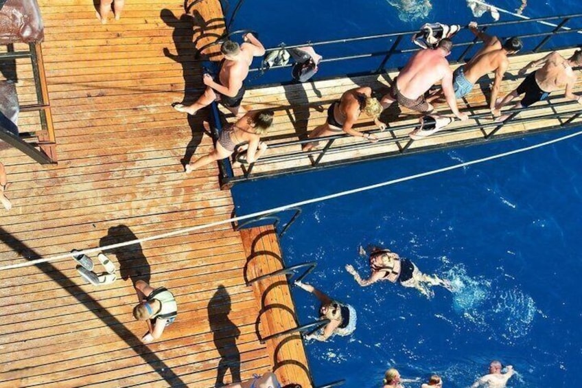 A group of people on a wooden deck by a pool, some standing and some swimming. 2