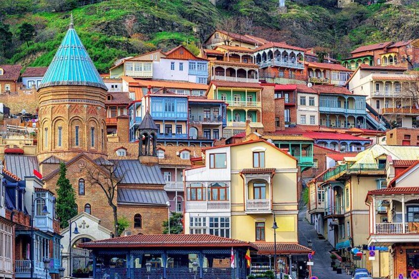 A densely packed hillside town with colorful buildings, a prominent church with a blue dome, and a steep street. 2