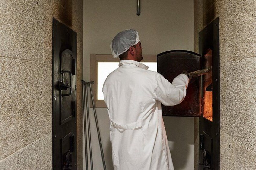 Una persona con uniforme de chef blanco y gorro de malla opera un horno de pizza. 4