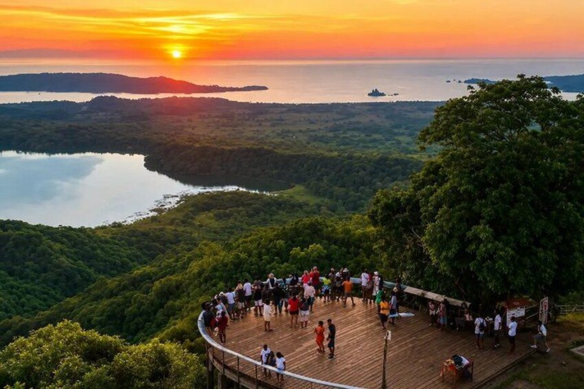 A sunset over a forested landscape with a wooden viewing platform and people gathered around. 4