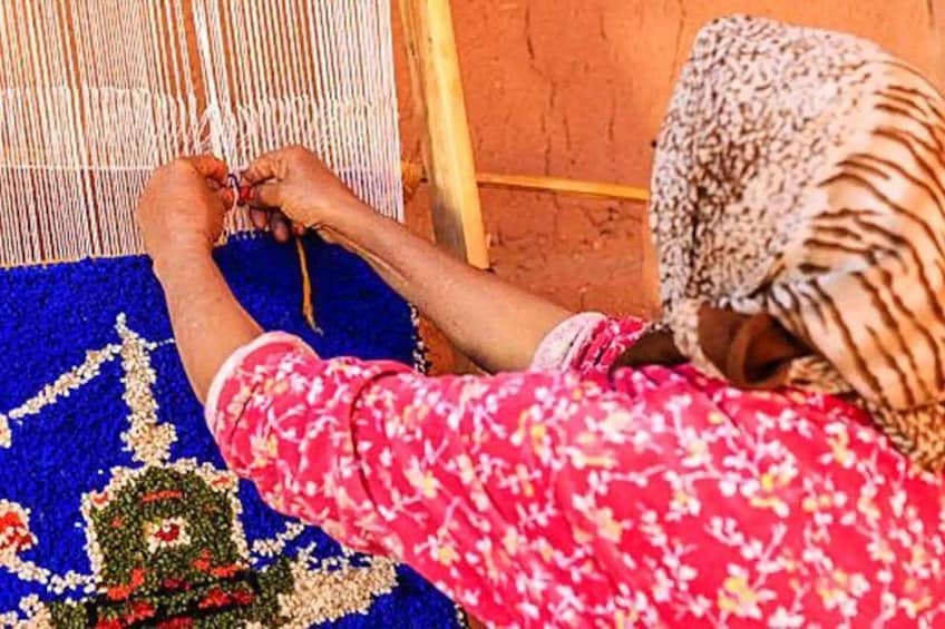 A person weaving on a loom with a blue patterned fabric. 2