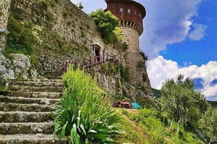 A stone staircase leading to a tower with a round top, surrounded by greenery and a clear sky. 3