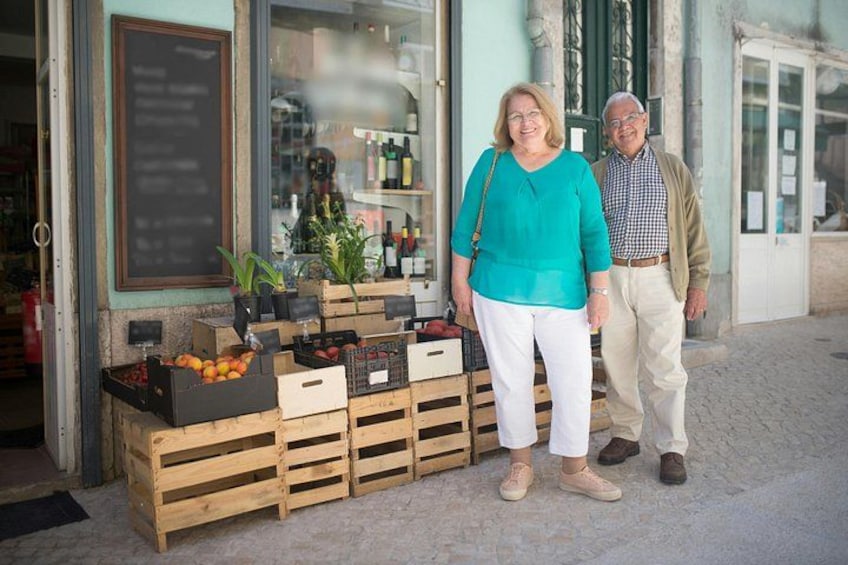 A storefront with wooden crates of fruits and vegetables, a potted plant, and a person standing in front. 2