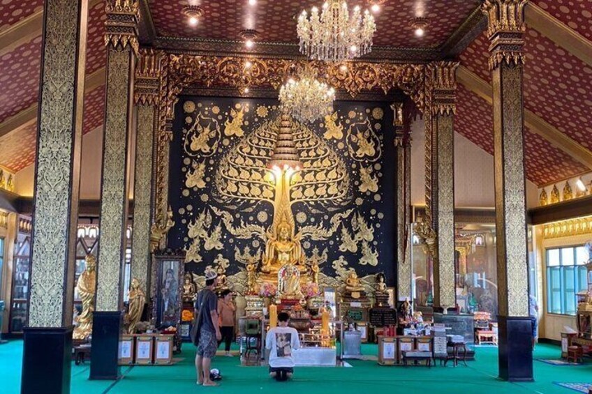 Ein aufwendig gestalteter Innenraum mit einer großen, goldenen Buddha-Statue, filigranen Wandreliefs und einem Kronleuchter. 3