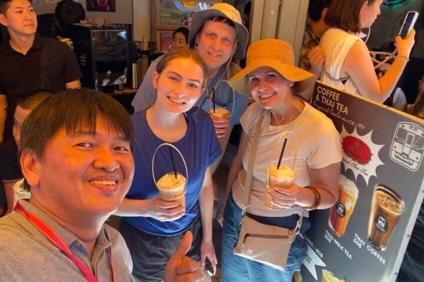 Een groep mensen in een café met drankjes en een menukaart waarop koffie en Thaise thee staan aangeboden. 2