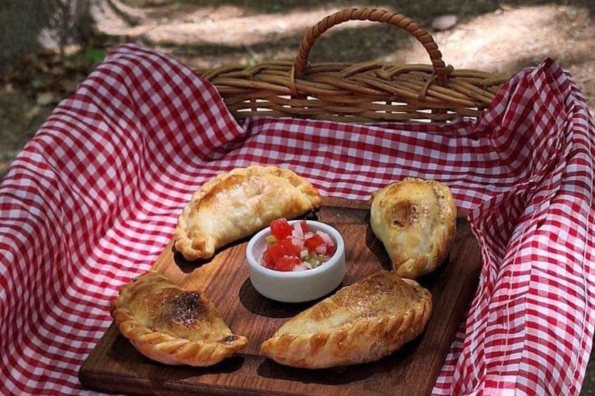 En picknickuppsättning med en rutig duk, en träbricka med bakverk och en liten skål med sås. 3