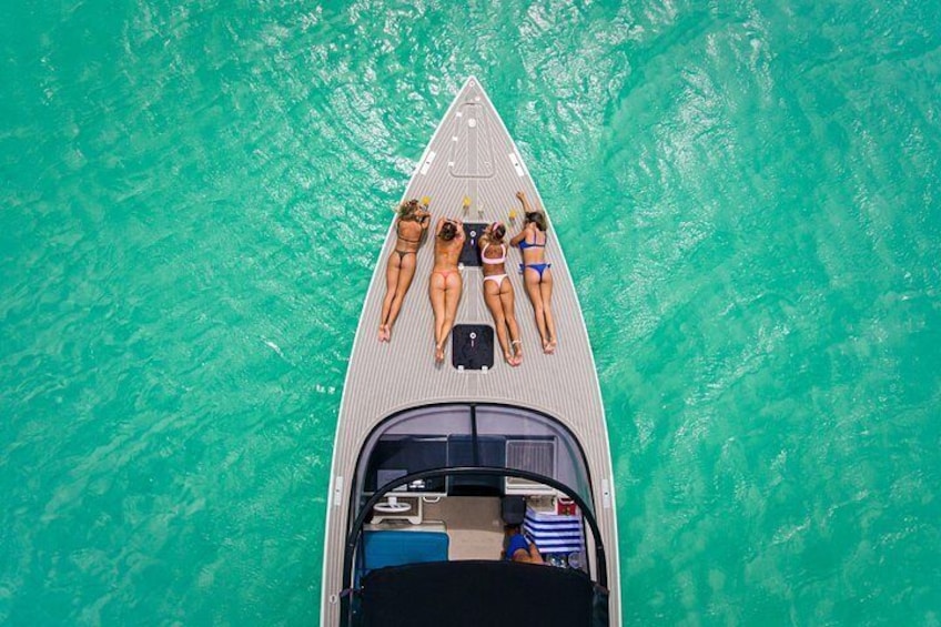 A boat with three people lying on the deck, surrounded by turquoise water. 4