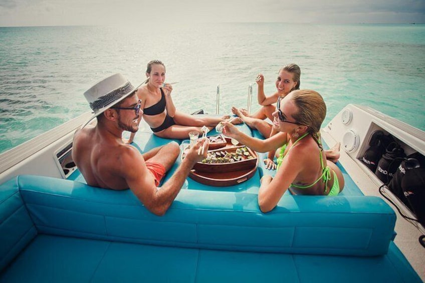 A group of people on a boat with a blue cushioned seating area, enjoying drinks and a meal. 2