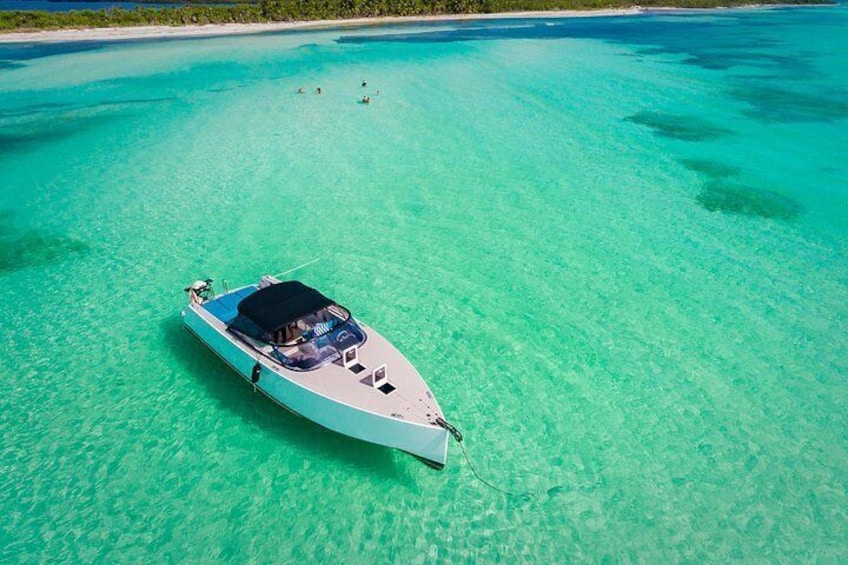 A boat anchored in clear turquoise waters with a sandy beach and greenery in the background. 5