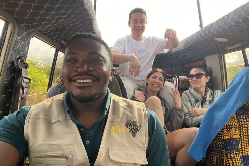 A group of people on a safari vehicle with a netted roof, surrounded by greenery. 2
