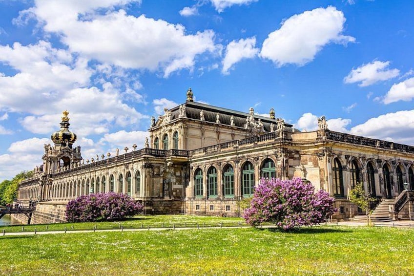 Un edificio histórico imponente con arquitectura ornamentada, una cúpula grande y un jardín cuidado con flores moradas. 3