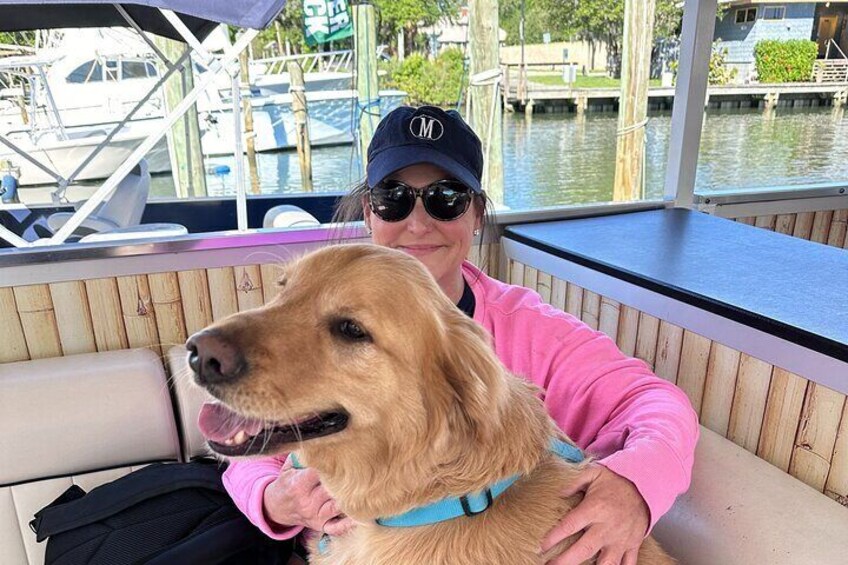 A person in a pink jacket holding a dog on a boat with a dock and water in the background. 5