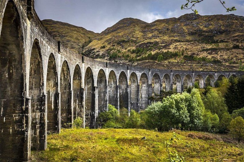 Un viaducto de piedra con múltiples arcos, rodeado de vegetación verde y colinas al fondo. 1