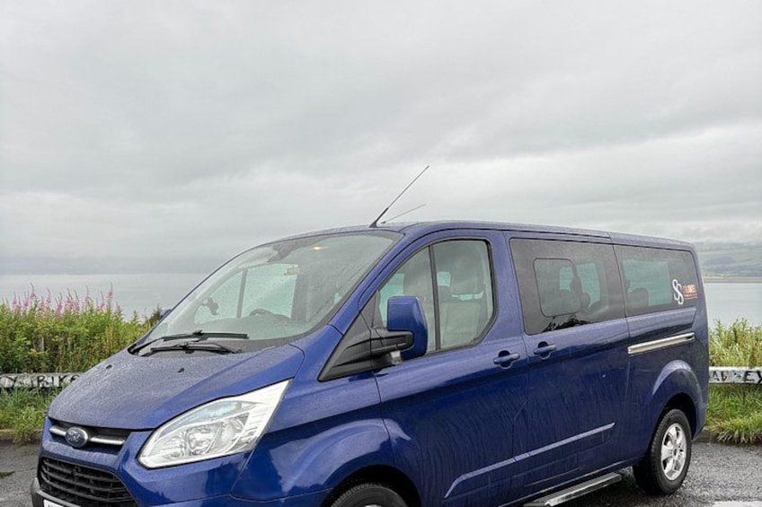 Una camioneta azul estacionada al costado de una carretera, con una masa de agua y vegetación al fondo. 3