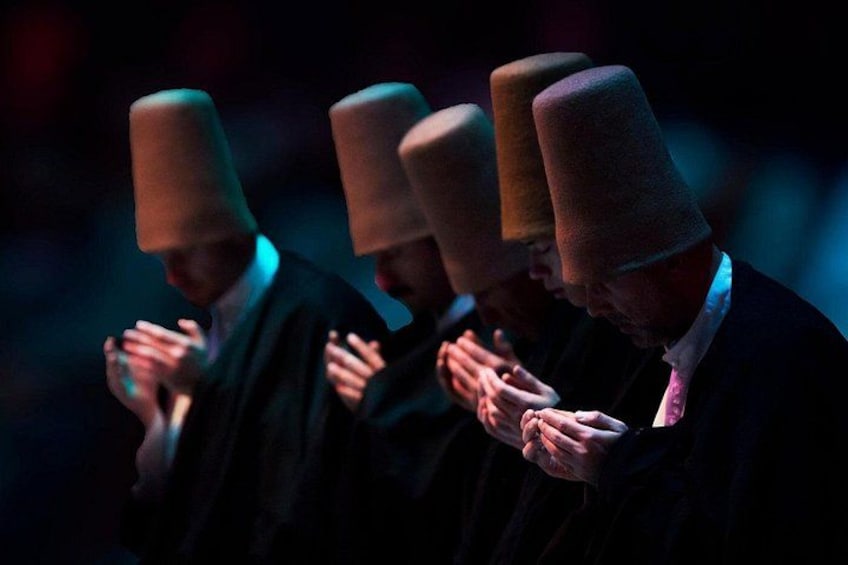 Un grupo de personas vestidas de oscuro con sombreros altos y cónicos, de pie en fila con las manos unidas. 4