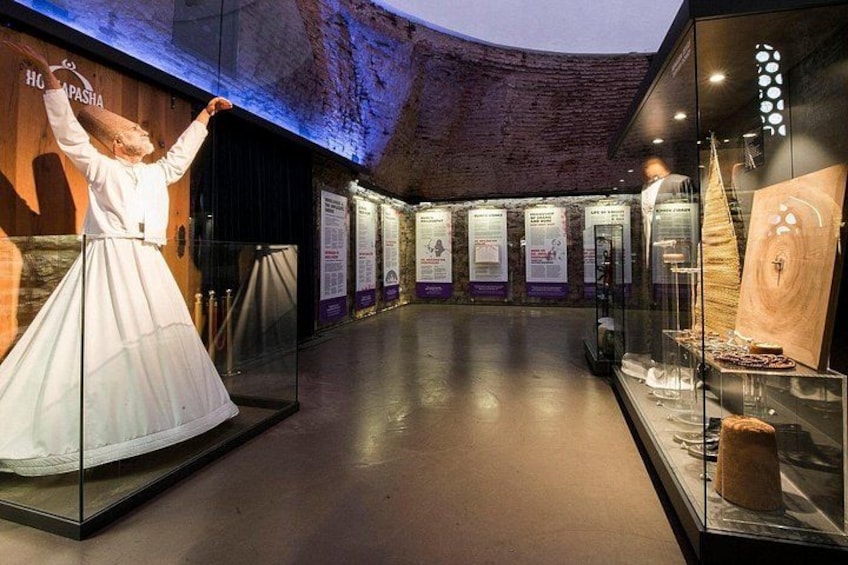 Una exhibición de museo con un maniquí vestido de blanco, vitrinas con artefactos y carteles informativos en la pared. 3