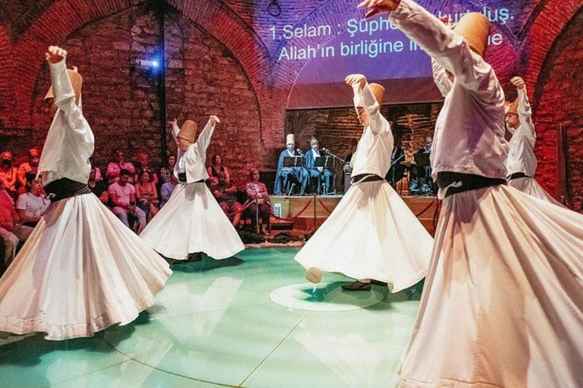 Un grupo de bailarines con atuendo blanco tradicional se presenta en un escenario con un público en el fondo. 2