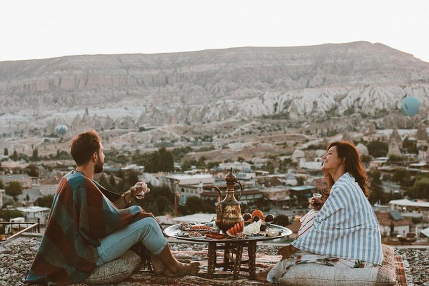 Deux personnes sont assises sur une couverture, devant une table où sont disposés de la nourriture et des boissons, et elles jouissent d’une vue sur un paysage montagneux. 5