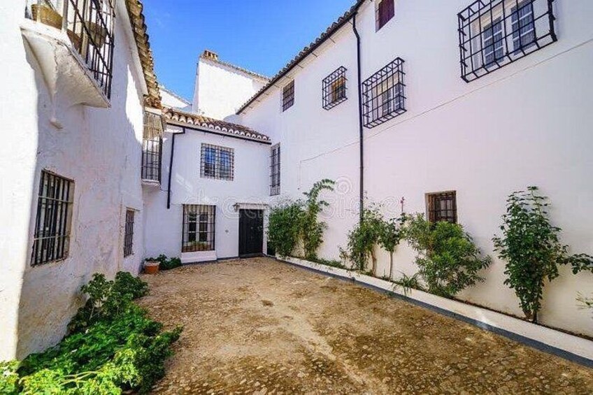 A courtyard with white buildings, a dirt ground, and some greenery. 5