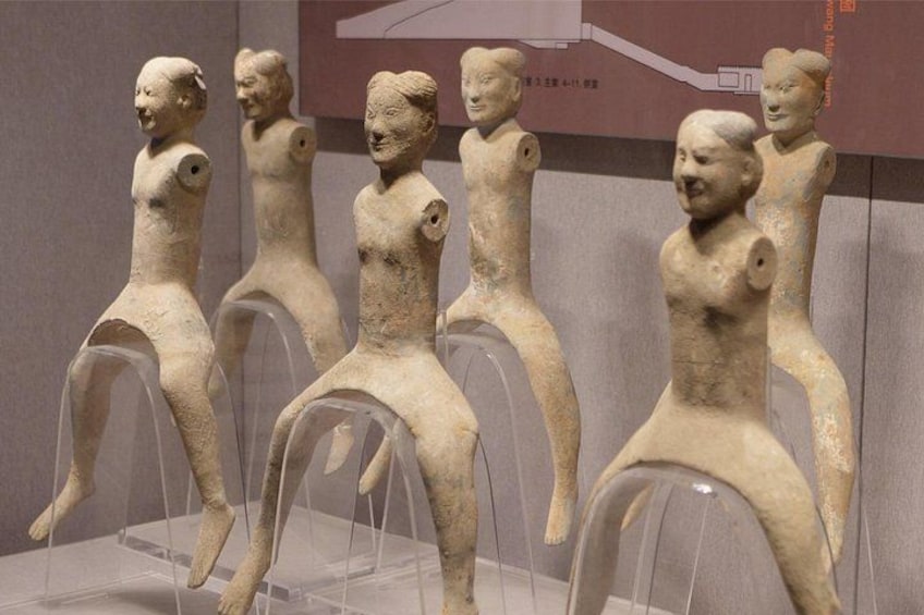 A collection of ancient terracotta figurines displayed on clear pedestals in a museum setting. 2
