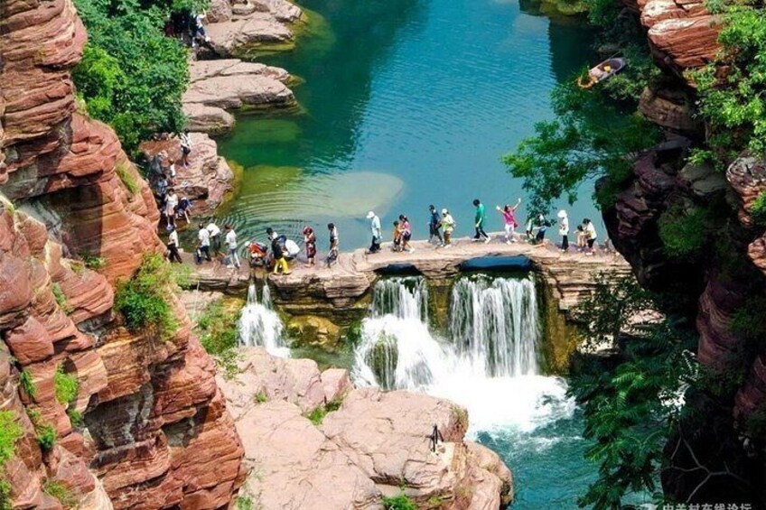 A group of people standing on a rock bridge over a waterfall in a canyon. 4
