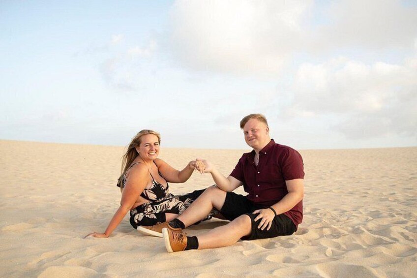 Two people sitting on a sandy beach with a clear sky. 5