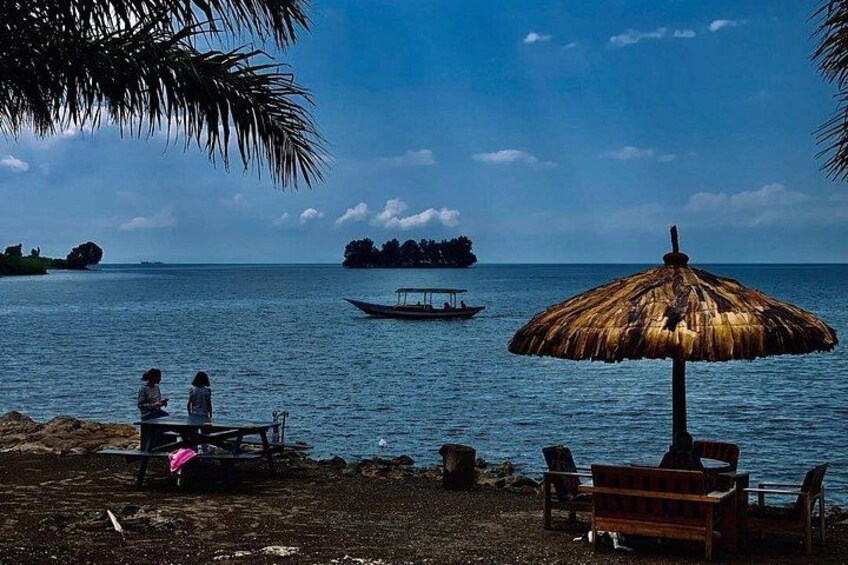 A beach with a thatched umbrella, a wooden bench, and a boat in the water. 1