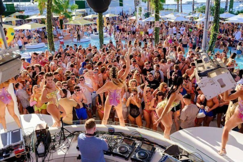 A crowded outdoor event with people dancing and a DJ booth. 3