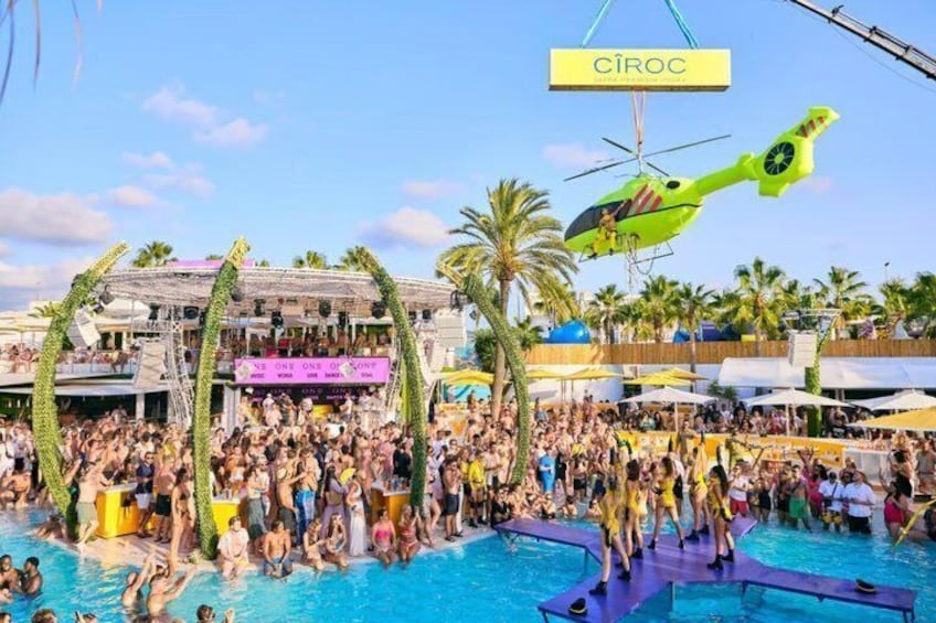 A crowded outdoor pool area with a helicopter and a building labeled 'CIROC' in the background. 4