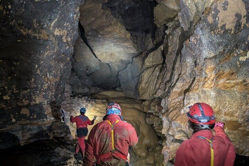 Trois personnes, vêtues de vestes rouges et portant des casques, se trouvent à l’intérieur d’une grotte aux parois rocheuses. 3
