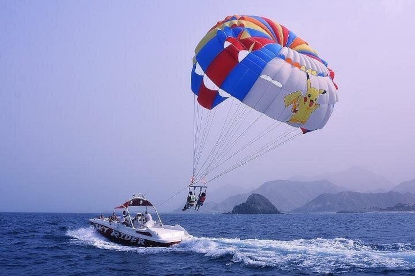 A parasailing activity with a colorful parachute, a boat, and a mountainous landscape in the background. 1