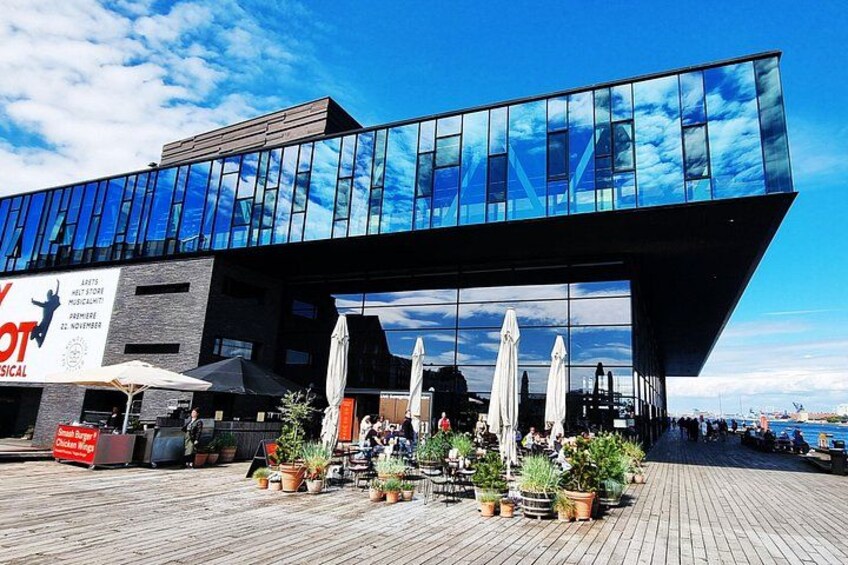 Un bâtiment moderne avec une façade en verre, un espace extérieur aménagé avec des parasols et des plantes en pot. 3