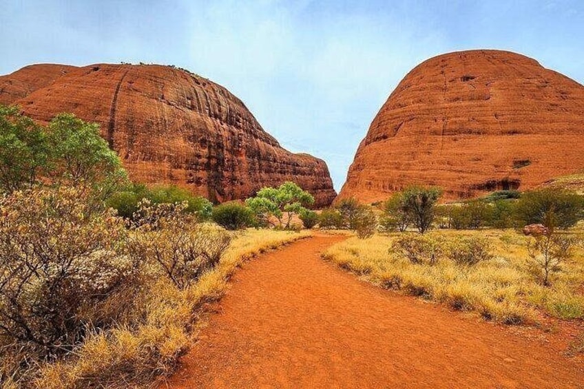 A dirt path leading through a desert landscape with two large red rock formations. 2