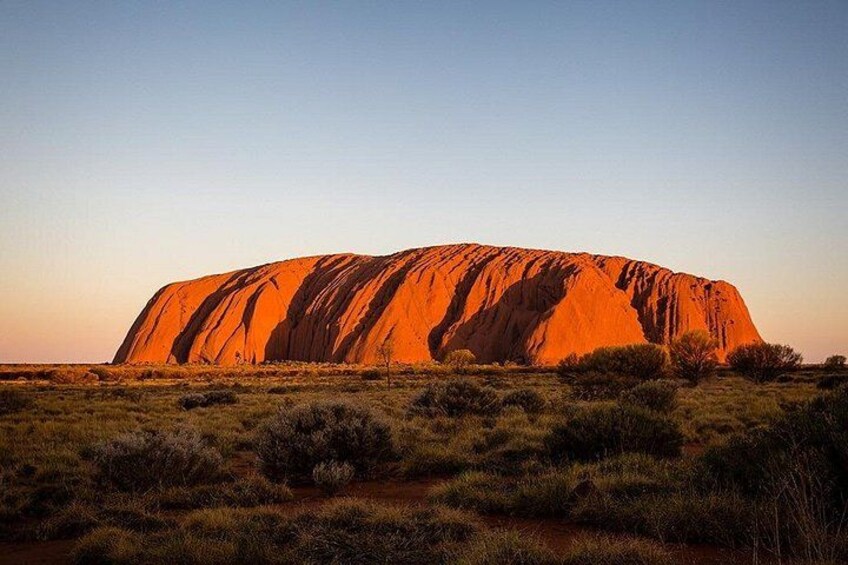 Uluru at sunset with surrounding sparse vegetation. 3