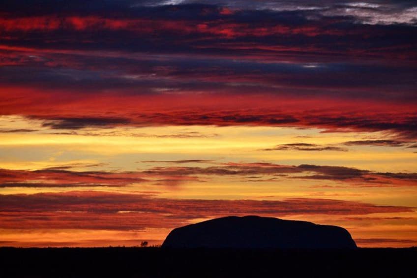 A sunset with a silhouette of a large rock formation against a colorful sky. 1