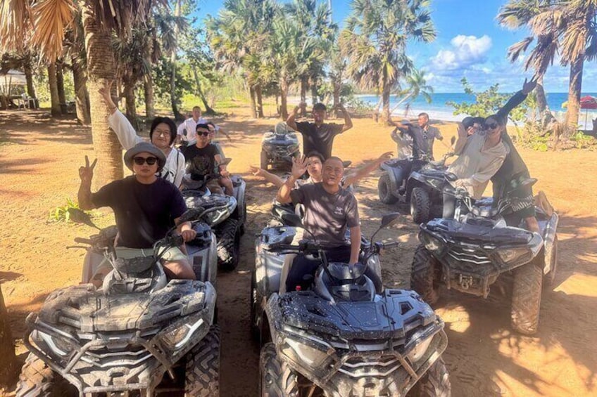 A group of people on ATVs on a sandy path with palm trees and a beach in the background. 1