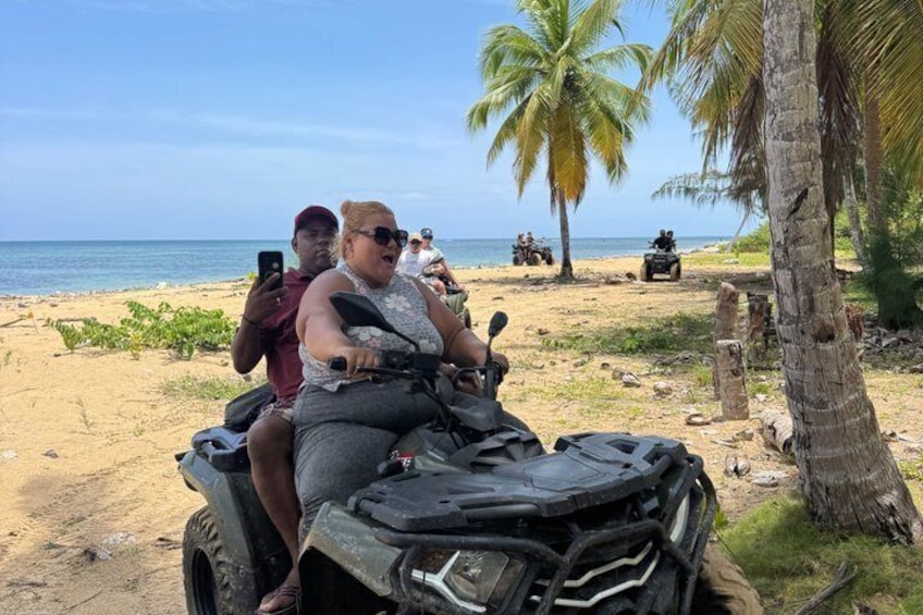 En person kører på en ATV på en sandstrand med palmer og hav i baggrunden. 5