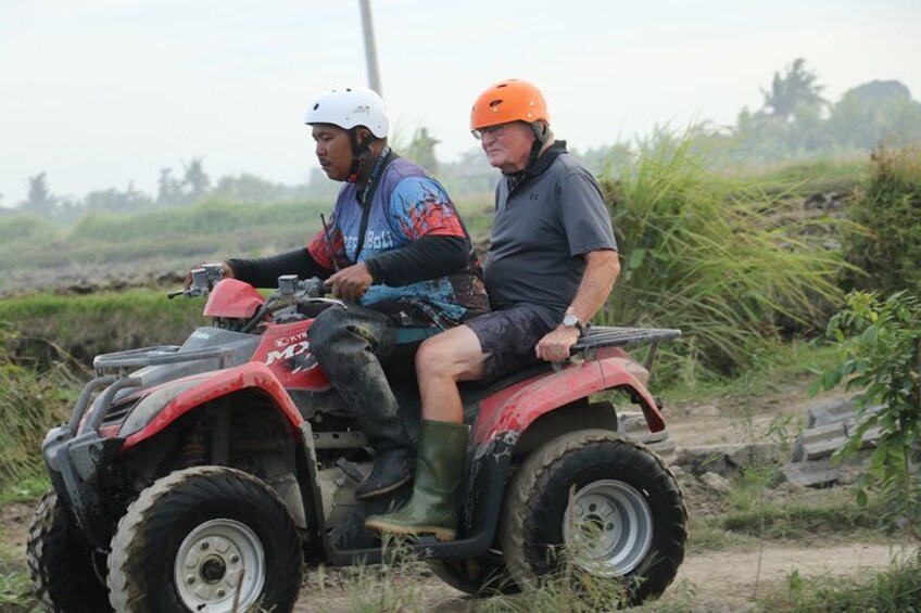 Two people on a red ATV in a rural setting with vegetation. 4