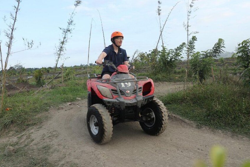 A person riding a red ATV on a dirt path surrounded by vegetation. 3