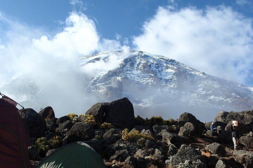 A mountain with snow, a clear sky, and a person standing on a rocky outcrop. 3