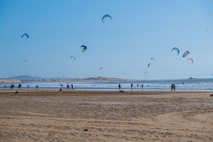 Ein Strand mit Menschen, die Drachen steigen lassen, und einem wolkenlosen Himmel. 4